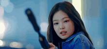 a woman in a denim jacket is holding a gun in her hand .