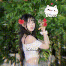 a girl with a flower in her hair is standing in front of a tree holding a flower in her hand .
