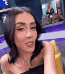 a woman wearing a black top and a necklace is sitting on a couch