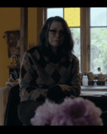 a woman sitting in front of a window wearing a plaid sweater