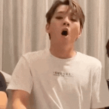a young man wearing a white t-shirt is making a funny face .