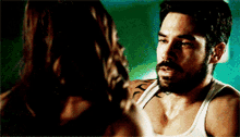 a man with a beard and a tattoo on his chest talks to a woman