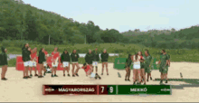 a group of people standing on a sandy beach with a scoreboard that says " magyarország " and " mexiko "