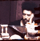 a man with a beard is sitting at a table with his hand on his chin