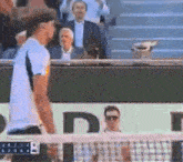 a man in a white shirt is standing in front of a tennis net with the number 46 on it ..