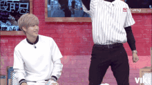 a man in a striped shirt stands next to another man in a white shirt with the word viki on the bottom