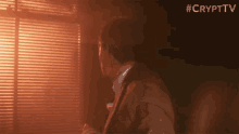 a man in a suit is standing in front of a window with blinds and the words #crypttv above him .