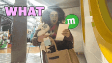 a woman holding a stuffed animal in front of a green m & m sign