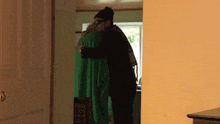 a man in a black hat and sunglasses is hugging a woman in a green sweater