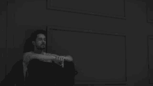 a man with a beard is sitting on the floor in front of a white wall