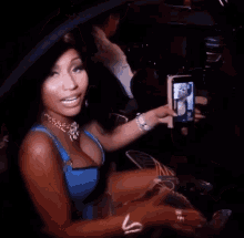 a woman in a blue top is taking a picture of herself on her phone .