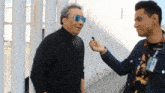 a man wearing sunglasses is being interviewed by a man wearing a name tag