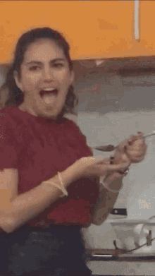 a woman in a red shirt is making a funny face while holding a spoon .