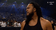 a man with long hair and a beard is standing in front of a crowd at a wrestling match .