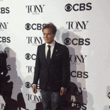 a man in a suit and tie stands in front of a wall that says tony on it