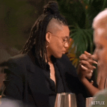 a woman with dreadlocks is holding another woman 's hand while sitting at a table with other people .