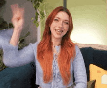 a woman with red hair is sitting on a couch raising her fist in the air .