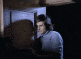 a man in a blue sweater stands in front of a wooden door