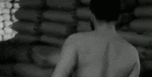 a black and white photo of a shirtless man standing in front of a pile of barrels .