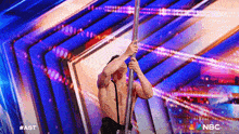 a pole dancer performs on a stage with a nbc logo behind him