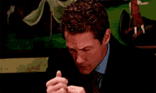 a man with curly hair is coughing while sitting at a table .