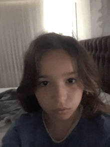 a young girl in a blue shirt is taking a selfie in front of a bed