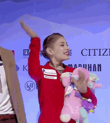 a woman in a red jacket is holding a stuffed animal in front of a sign that says citiz