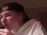 a woman wearing a baseball cap and a white hoodie is eating a piece of food .