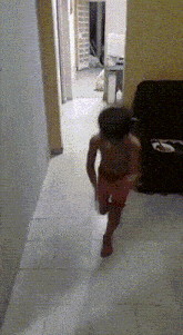 a little boy in red shorts is running down a hallway towards a couch