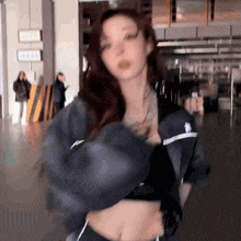 a woman wearing a crop top and a jacket is standing in a room .