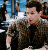 a man in a plaid shirt and tie is sitting at a table in a room .