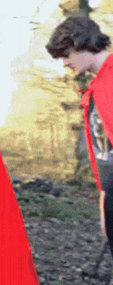 a man in a red cape is walking in the woods with a cane .