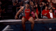 a man in a red and gray tank top with the word titan on it is screaming in front of a crowd .