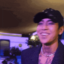 a man wearing a hat and a necklace with the word love on his chest smiles