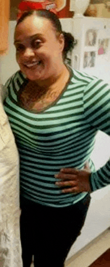 a woman in a green and black striped shirt is standing in front of a refrigerator in a kitchen .