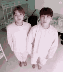two young men are standing next to each other in a room wearing white sweaters .