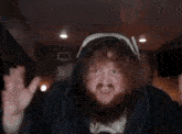 a man with a beard and curly hair is wearing a hooded jacket and making a funny face .