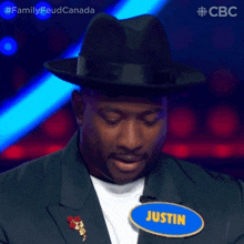 a man wearing a black hat and a suit is sitting in front of a blue sign that says passstin .