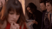 a group of people are standing in a room and one of them is looking at a piece of paper .