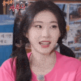 a close up of a girl with pigtails wearing a pink shirt and smiling .