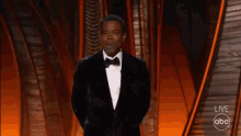 a man in a tuxedo is walking on a stage at a live abc show
