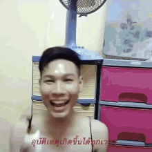 a man is laughing in front of a fan and a pink dresser