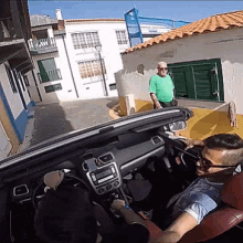 a man in a green shirt is standing behind a man in a car
