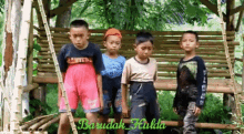 four young boys are standing in front of a wooden bench with the name barudak hulda written on the bottom