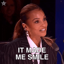 a woman in a suit and tie is smiling while sitting in front of a microphone and saying it made me smile .