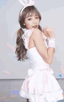 a woman in a pink dress and bunny ears makes a heart with her hands