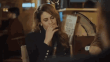 a woman is sitting at a table drinking from a cup