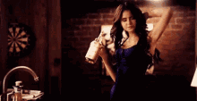 a woman in a blue dress is holding a bottle of whiskey in a dark room .