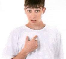 a young man wearing a white shirt is pointing to his chest
