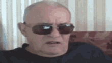 an elderly man wearing sunglasses is sitting on a couch .